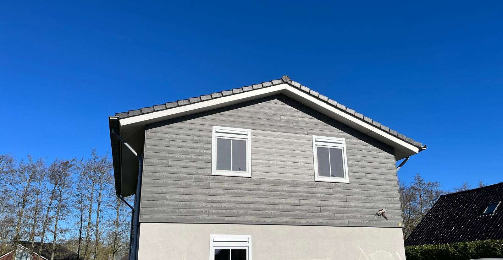 Wohnhaus mit grauer Fassadenverkleidung im Obergeschoss unter blauem Himmel