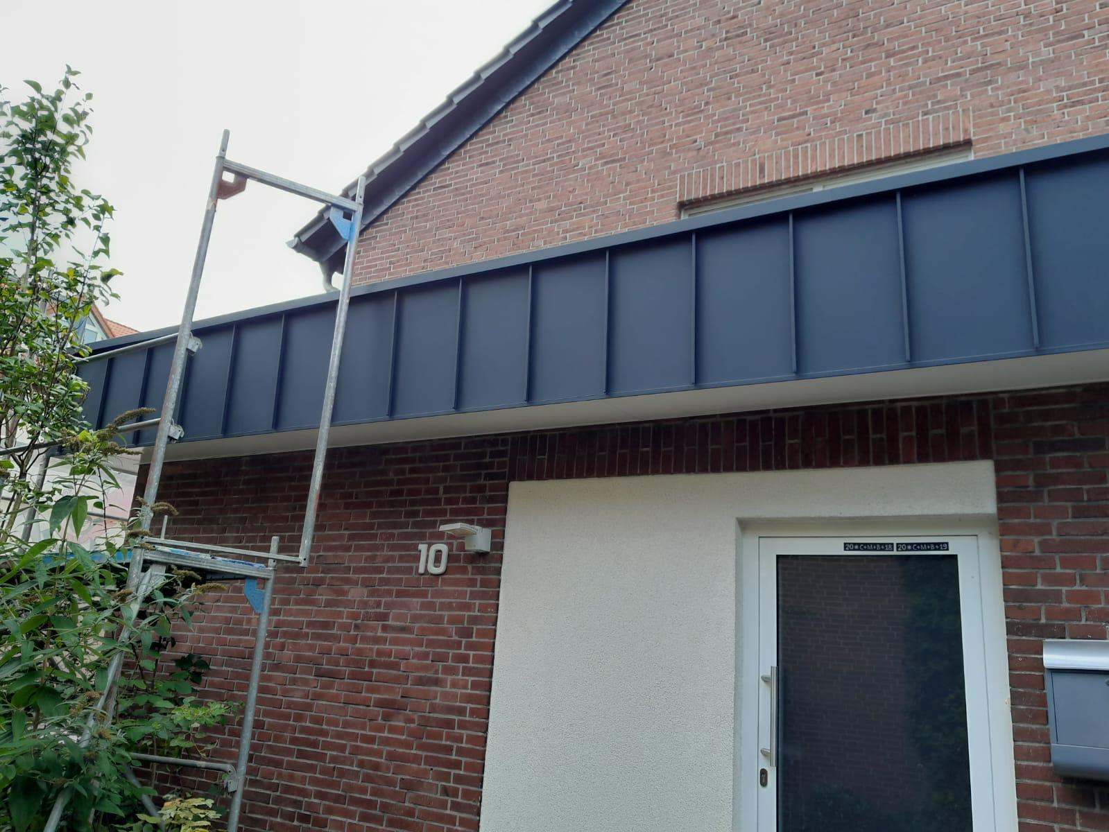 Anthrazitfarbene Metallverkleidung an einem Backsteinhaus