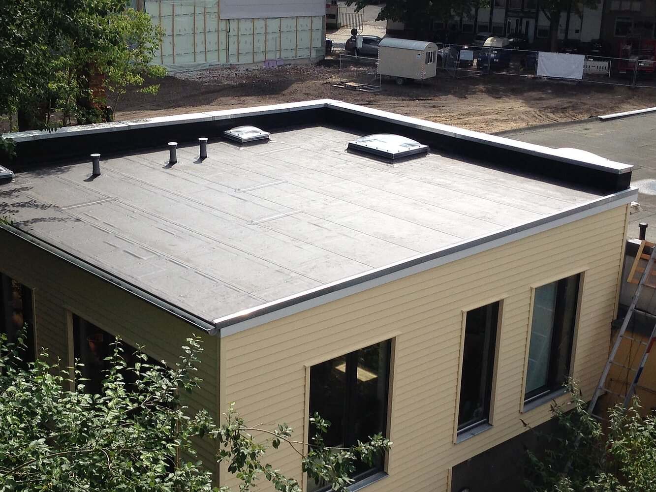 Flachdach mit Bitumenabdichtung, Randabschluss aus Metall und Lichtkuppel auf einem Haus mit heller Holzverkleidung