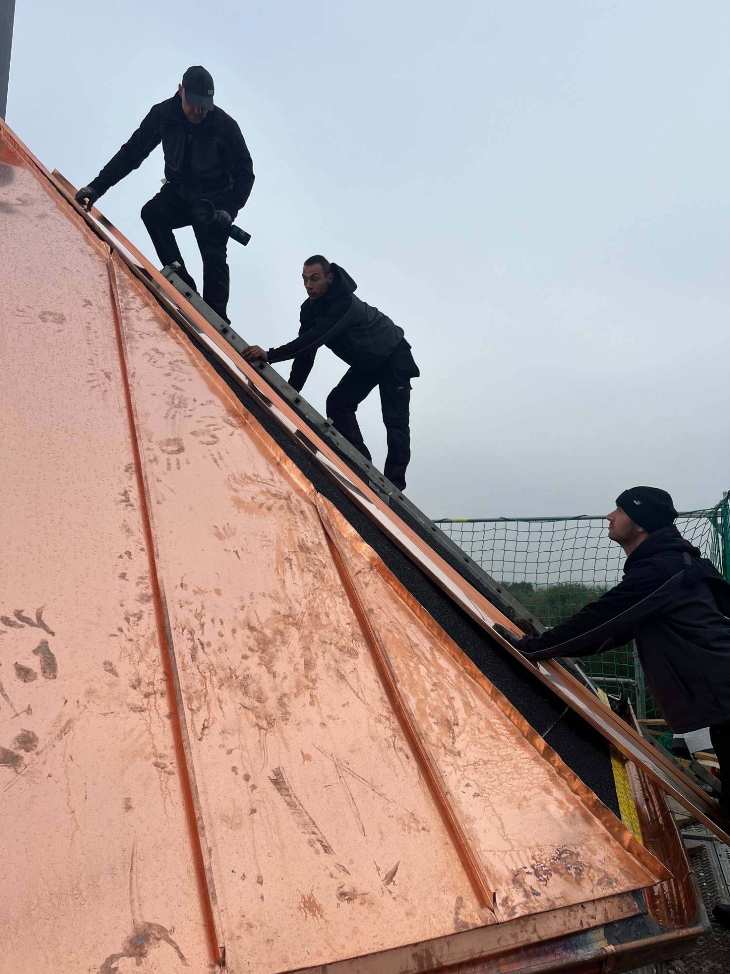 Handwerker bei der Montage einer Kupferdeckung auf einem steilen Dach