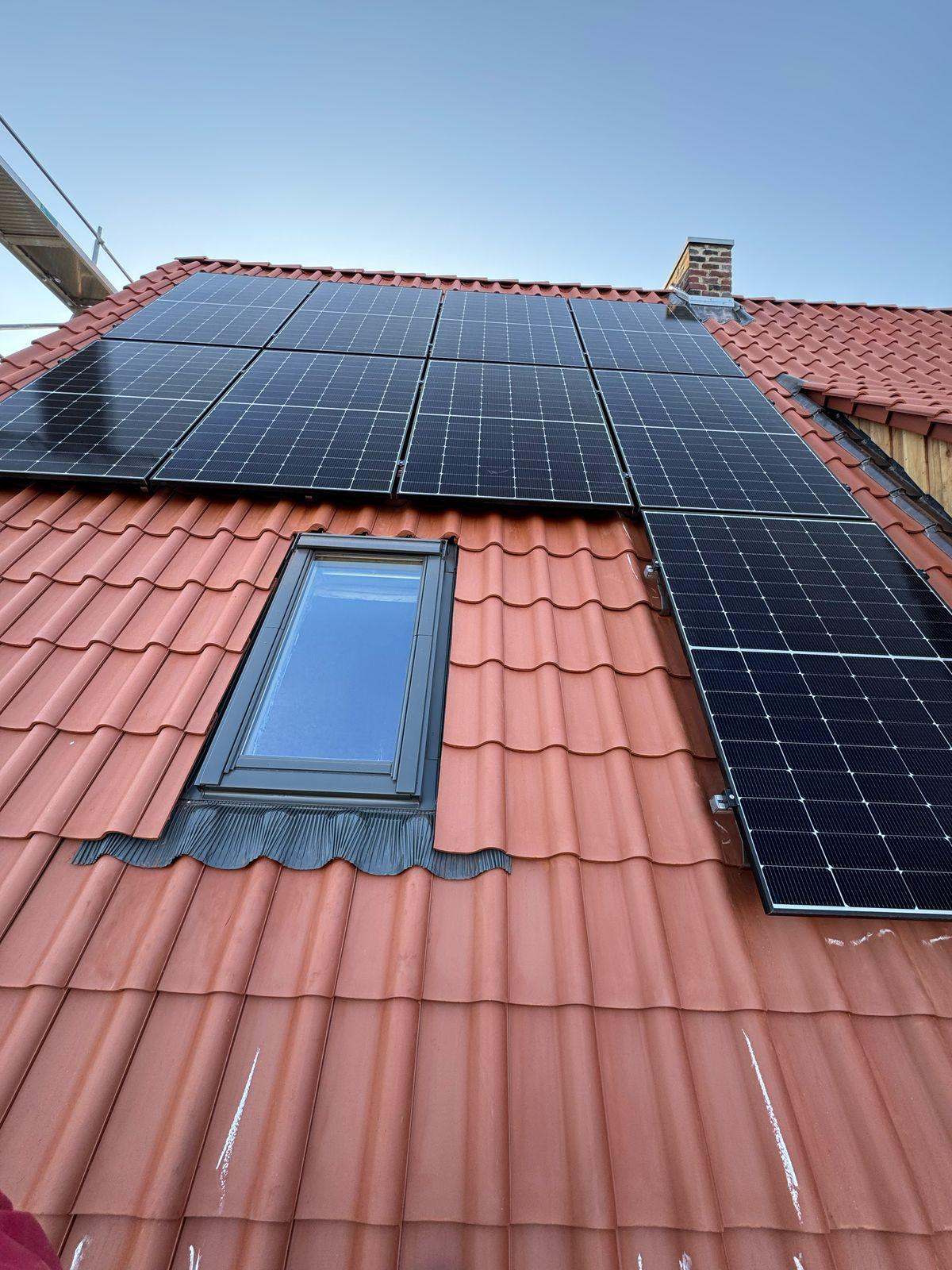 Photovoltaikmodule und ein Dachfenster auf einem roten Ziegeldach