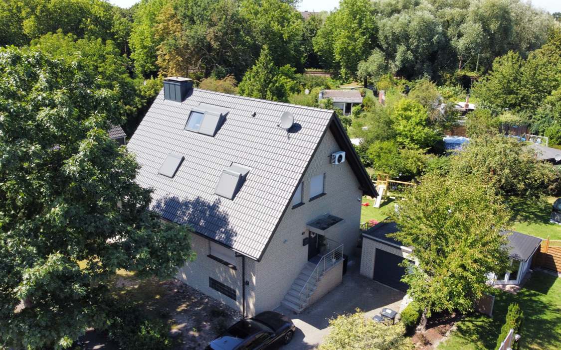 Wohnhaus mit grauem Satteldach, Dachfenstern und Schornstein, aus der Luft fotografiert
