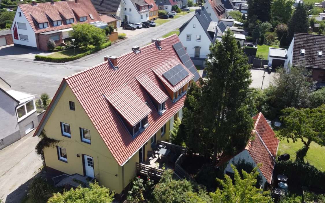 Rotes Ziegeldach eines gelben Wohnhauses mit Solarmodulen und Gauben